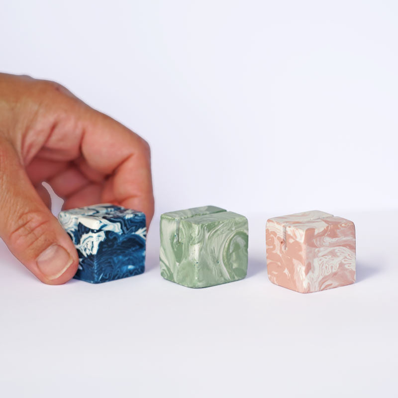 Three small square marble-patterned photo holders on a white surface with a hand reaching towards them