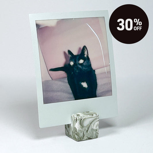 A square instant-film photo frame holder displaying a polaroid photo of a black cat, standing on a marbled cube base against a light grey background. A dark circular '30% OFF' sale badge appears in the top right corner.