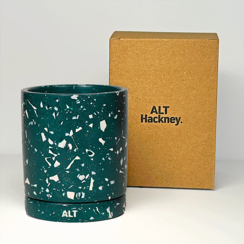 A dark teal green plant pot with a white terrazzo speckled pattern, shown next to its brown cardboard packaging box printed with the brand name 'ALT Hackney'.