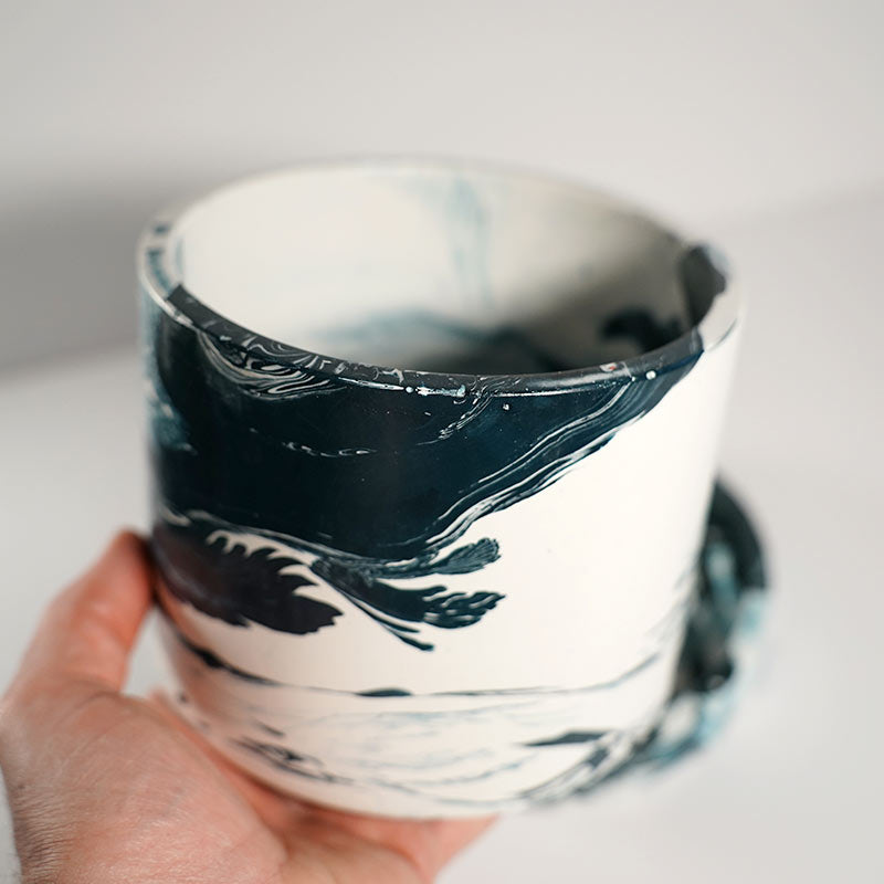 Hand holding a navy marble-patterned plant pot on a white background