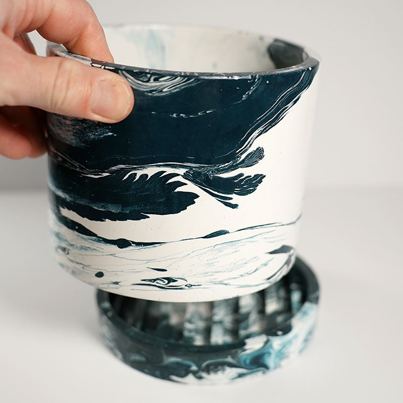 Hand holding a Navy marble-patterned plant pot on a white background