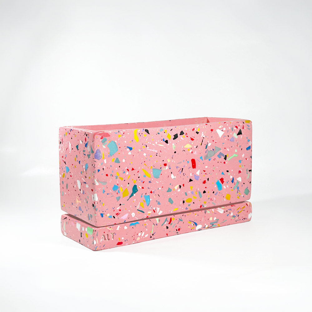 Pink rectangular plant pot with colourful speckles terrazzo with drainage holes and a water tray on a white background
