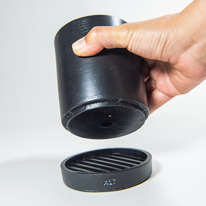 A hand holding a black Jesmonite plant pot with a separate water tray on a light gray background
