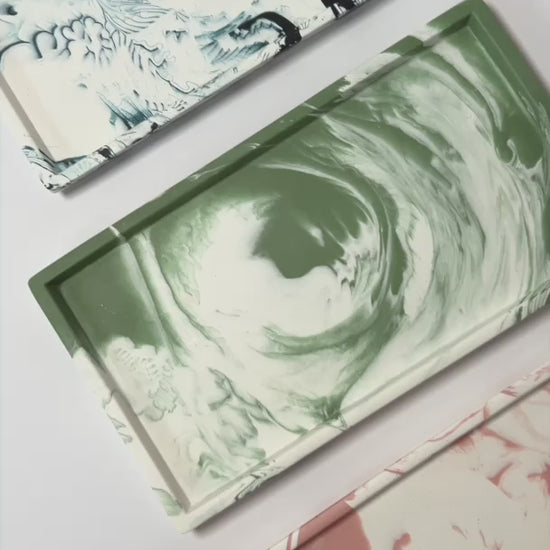 Three marbled decorative trays in moss green, salmon pink, and navy on a light grey background
