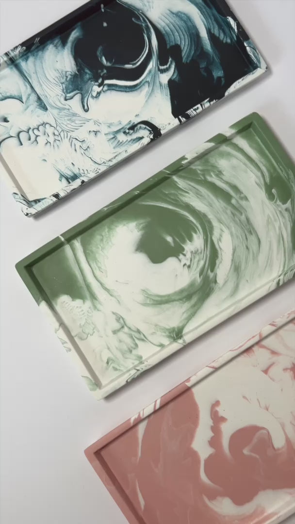 Three marbled decorative trays in moss green, salmon pink, and navy on a light grey background