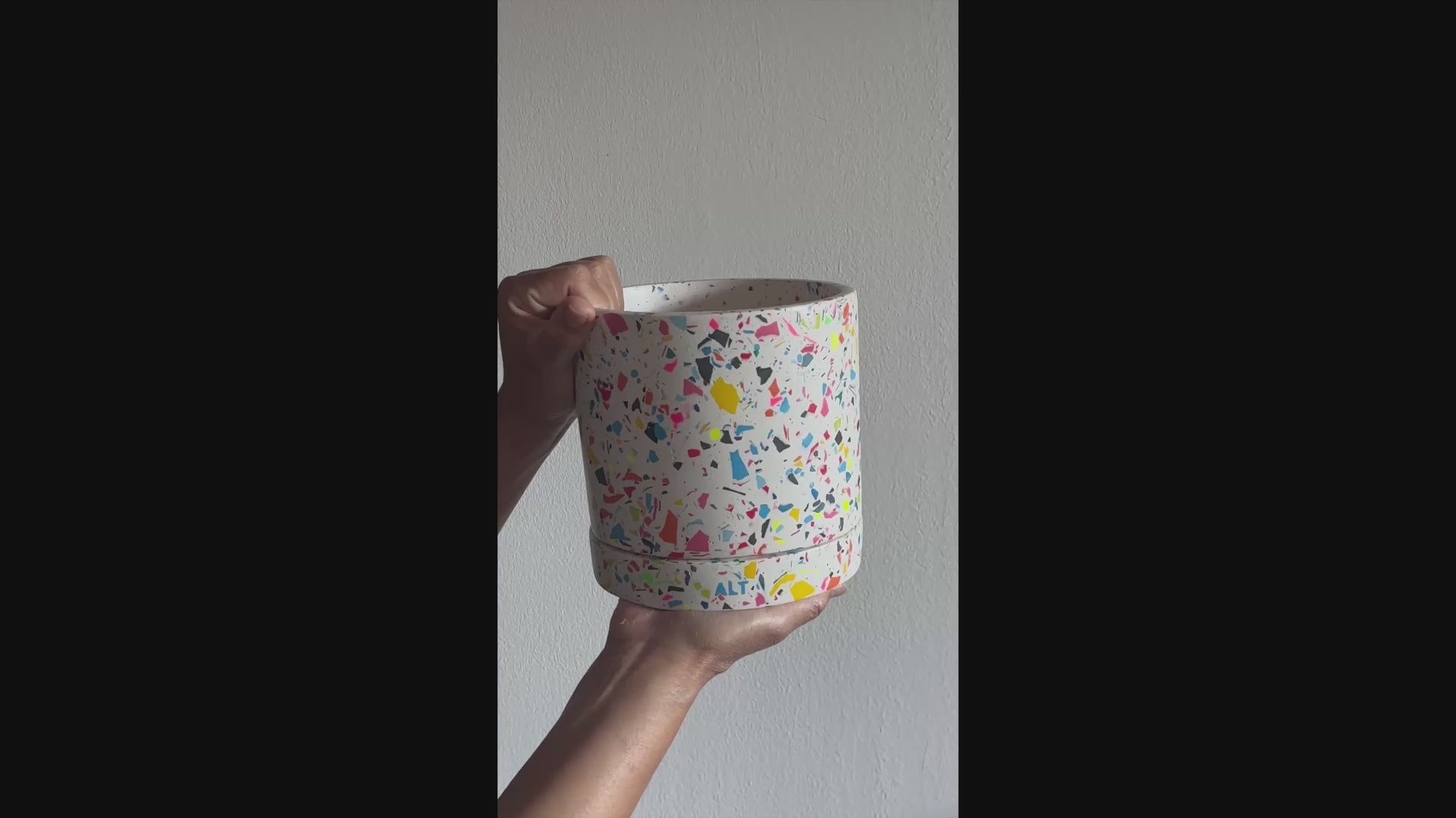 Hand holding a large rainbow terrazzo Jesmonite plant pot with drainage holes and matching water tray, a modern handmade indoor planter