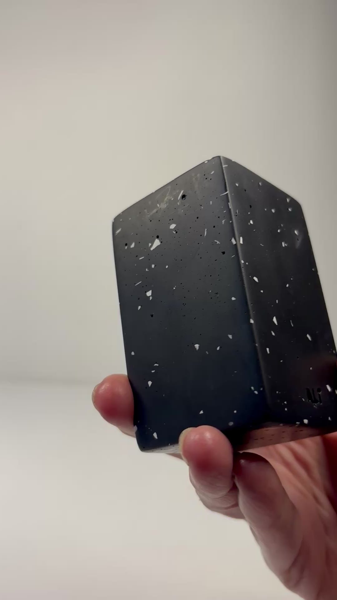 Hand holding a black with white terrazzo rectangular shaped tall tea light candle holder with a tea light candle inside on a plain background