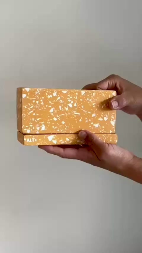 Hand holding a rectangular orange terrazzo Jesmonite plant pot with drainage holes and matching water tray, a modern handmade indoor planter for cactus and succulents.