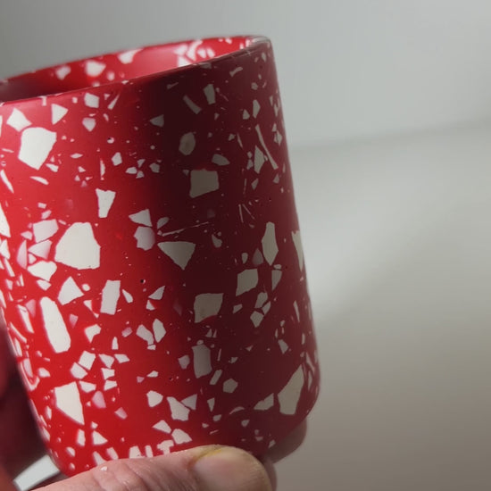 A hand holding a red terrazzo pen pot