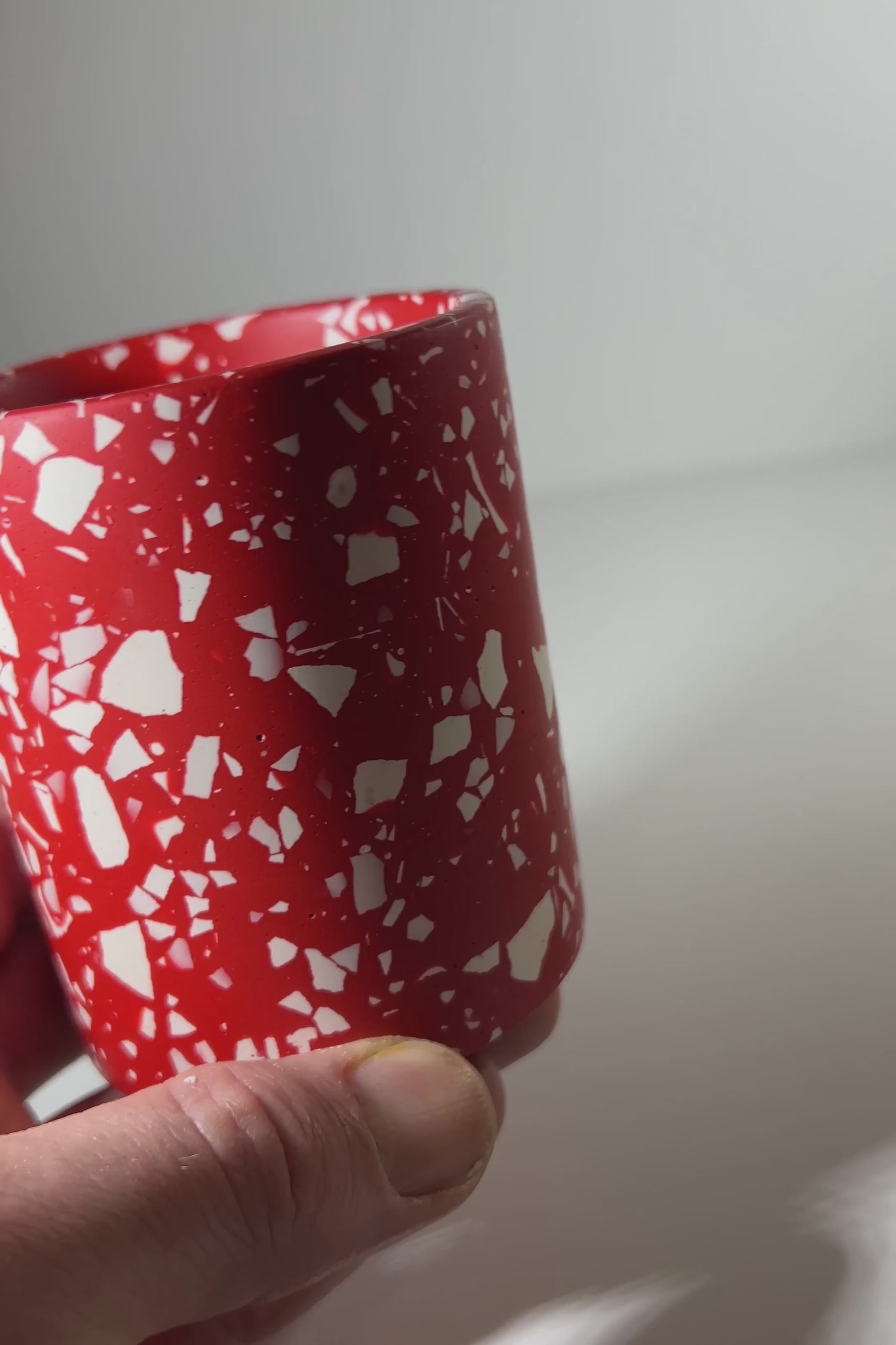 A hand holding a red terrazzo pen pot