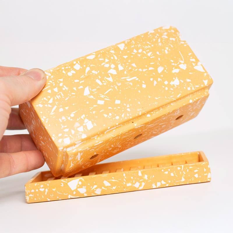 Hand holding a block of cheese-shaped soap with a white background