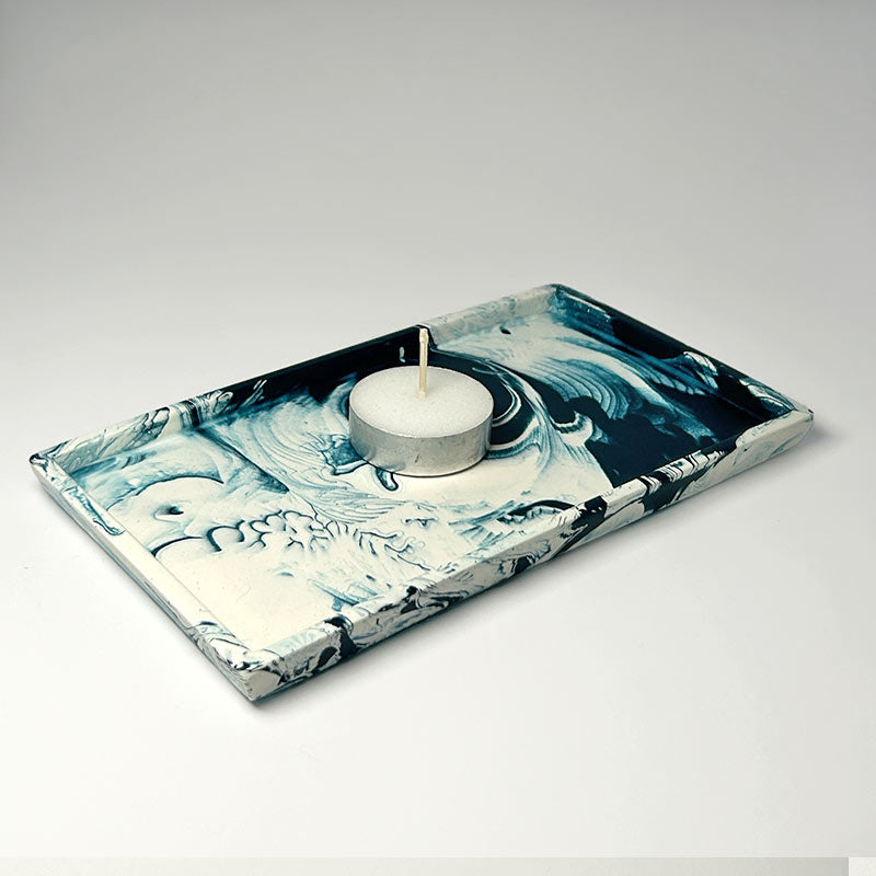 Decorative navy tray with a marbled design holding a candle on a light gray background
