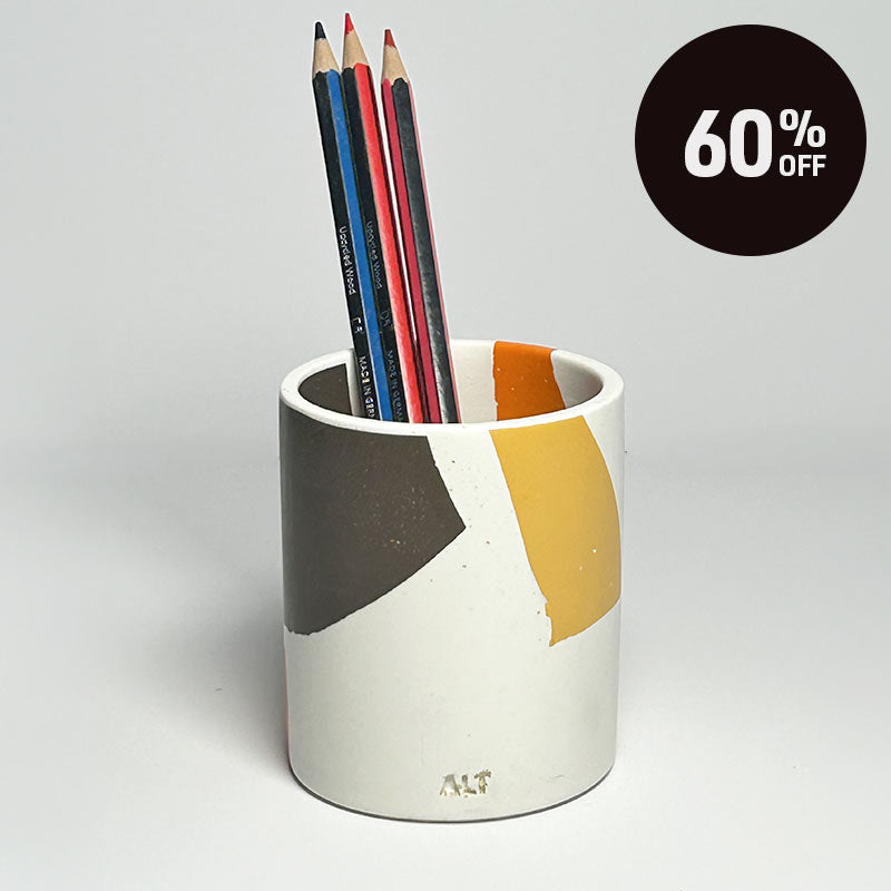 A white pencil holder with abstract geometric colour blocks in dark gray, mustard yellow, and orange, containing several pencils. A black circular '60% OFF' promotional sticker is in the top right corner.