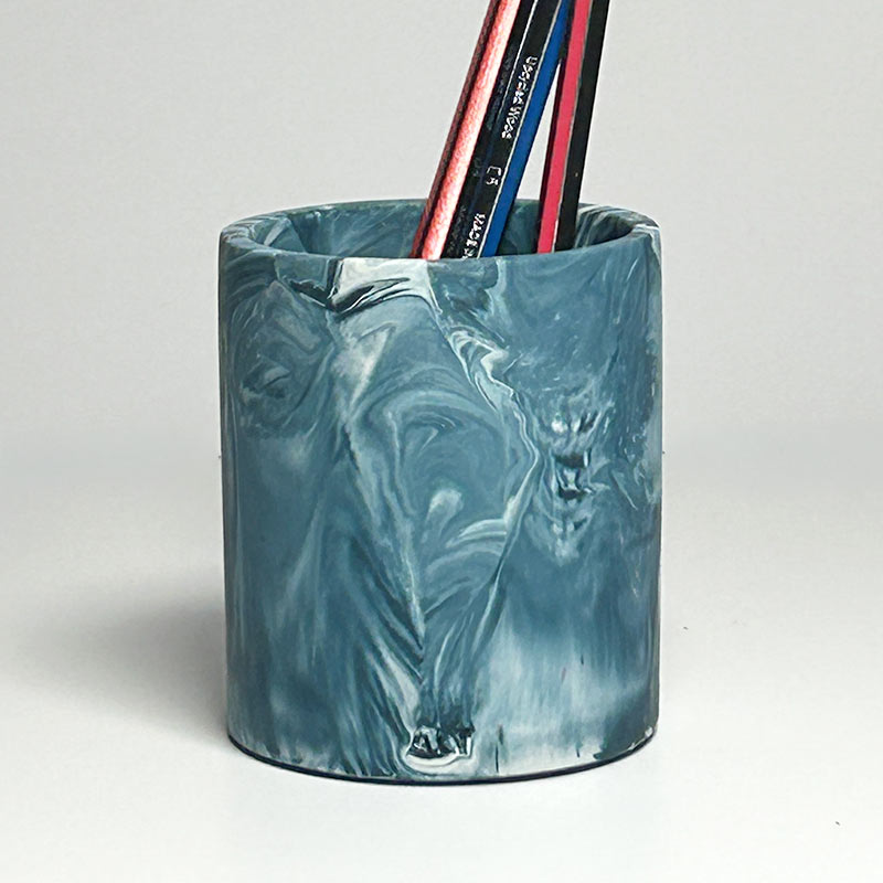 A cylindrical desk organizer cup with a marbled blue and white pattern, holding several pencils, on a light gray background.