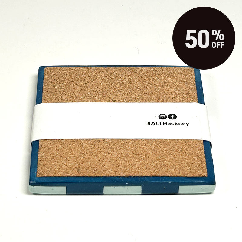A square cork board with a square coaster with a blue and mint green checkerboard pattern and a promotional badge with 50% off on top right corner