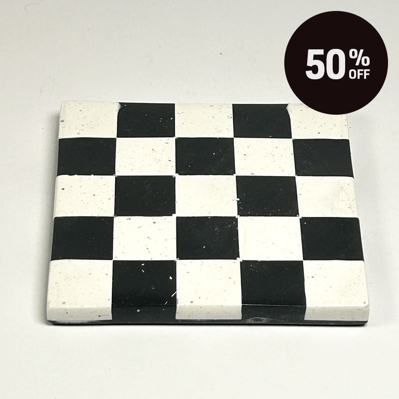 A square coaster with a black and white  checkerboard pattern and a promotional badge with 50% off on top right corner