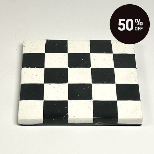 A square coaster with a black and white  checkerboard pattern and a promotional badge with 50% off on top right corner