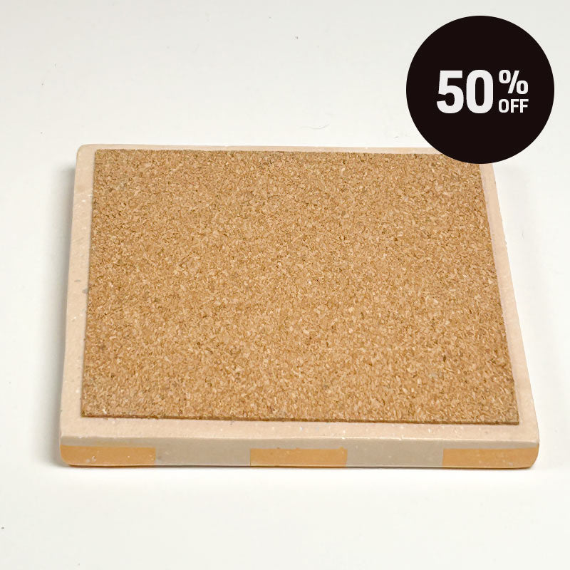 A square cork board with a square coaster with a pastel orange and beige checkerboard pattern and a promotional badge with 50% off on top right corner