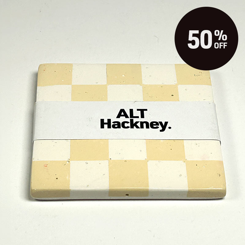 Warm beige and white checkerboard patterned coaster on a white background, wrapped in a white paper band labeled 'ALT Hackney.', on a light off-white background with a black '50% OFF' promotional sticker in the top right corner.
