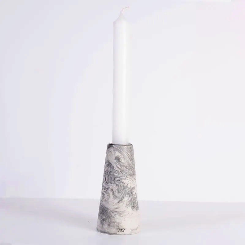 A white taper candle standing in a grey marble patterned tapered candle, shown on a white background 