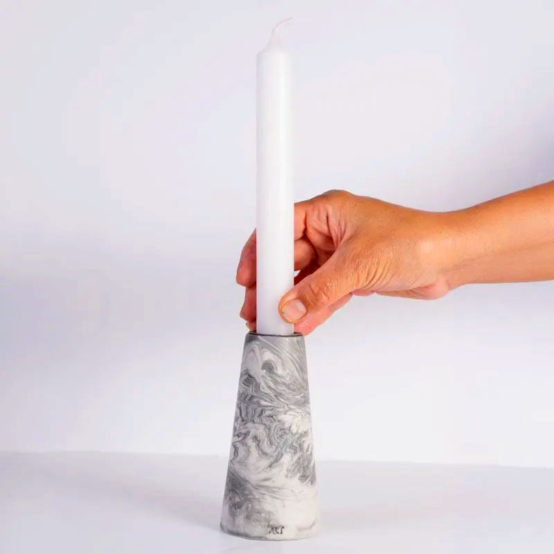 A hand holding a grey marble patterned tapered candle, shown on a white background 