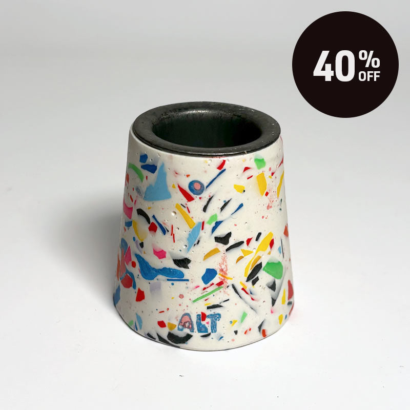 A small tapered taper candle holder with a terrazzo-style multicolour pattern on a white base, shown on a light grey background