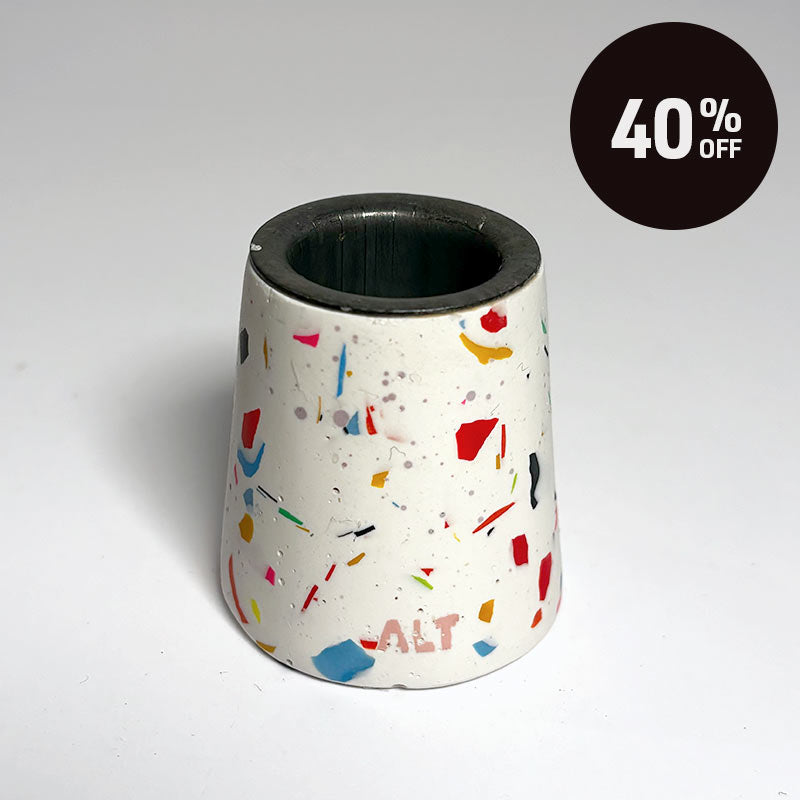 A small tapered taper candle holder with a terrazzo-style multicolour pattern on a white base, shown on a light grey background