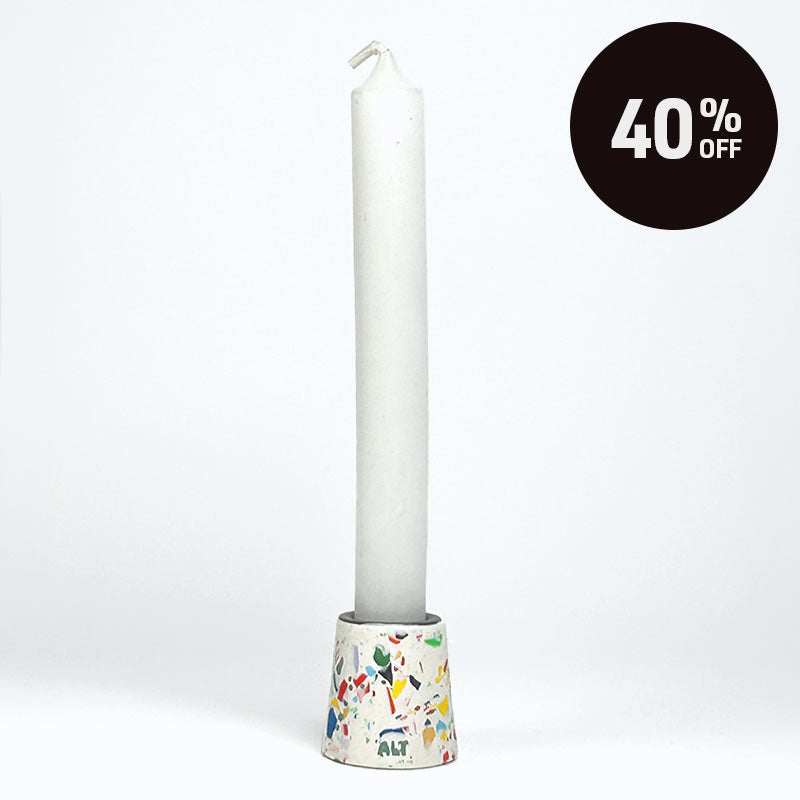 A small tapered taper candle holder with a terrazzo-style multicolour pattern with a long white taper candle on a white base, shown on a light grey background