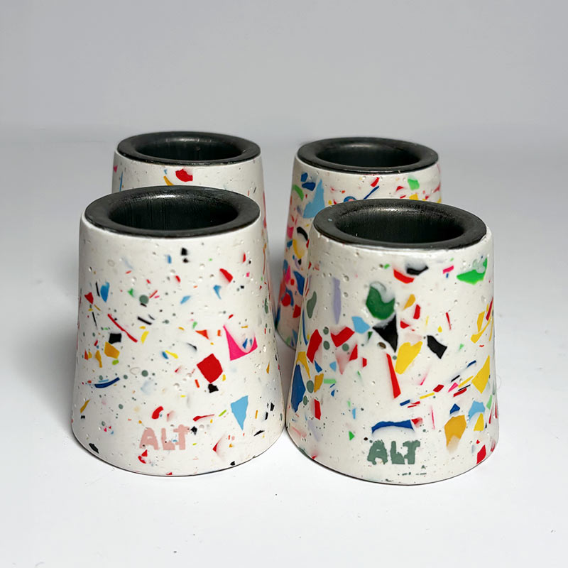 Four small terrazzo taper candle holders with colourful speckles on a white background.