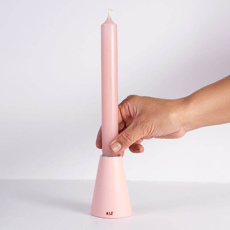 Hand holding a pink taper candle in a pink taper candle holder with a silver-toned top, shown on a white background