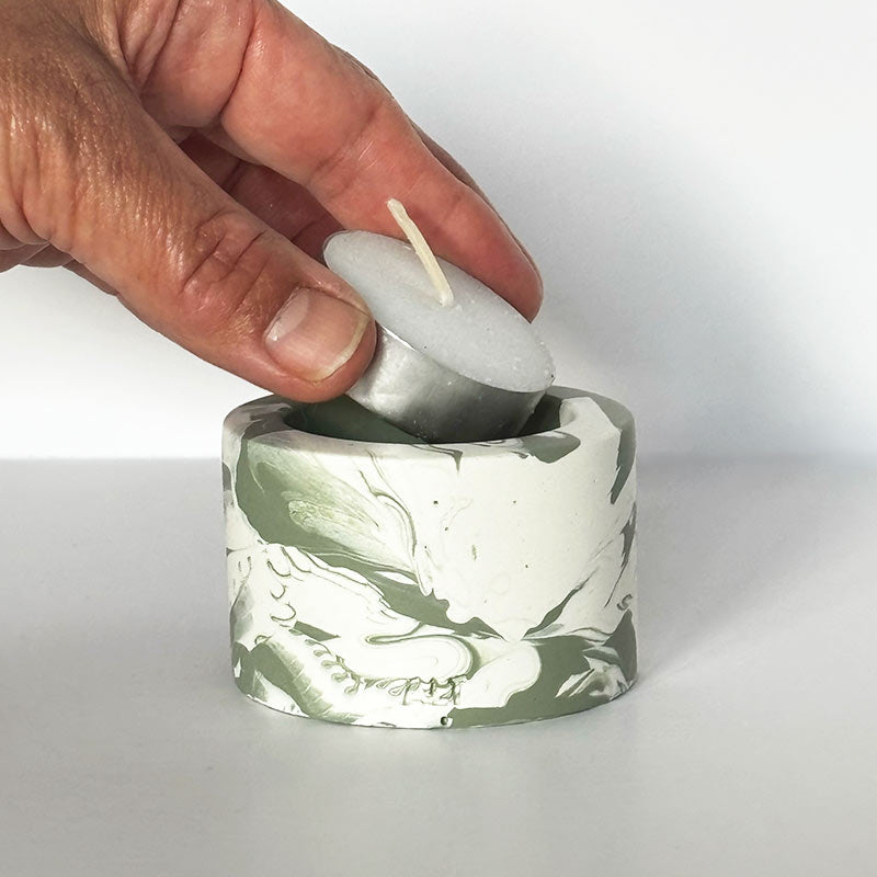 Hand placing a Moss Green Marble Jesmonite Tea Light Holder on a white background 
