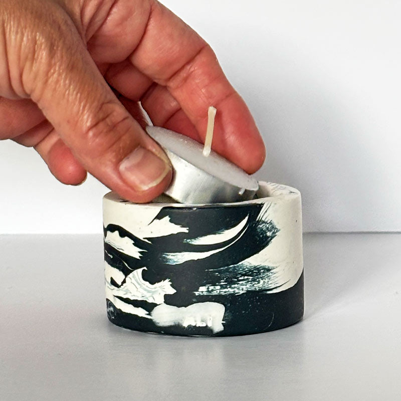 Marble-patterned navy and white tealight candle holder with a hand placing a tea light inside on a light gray background