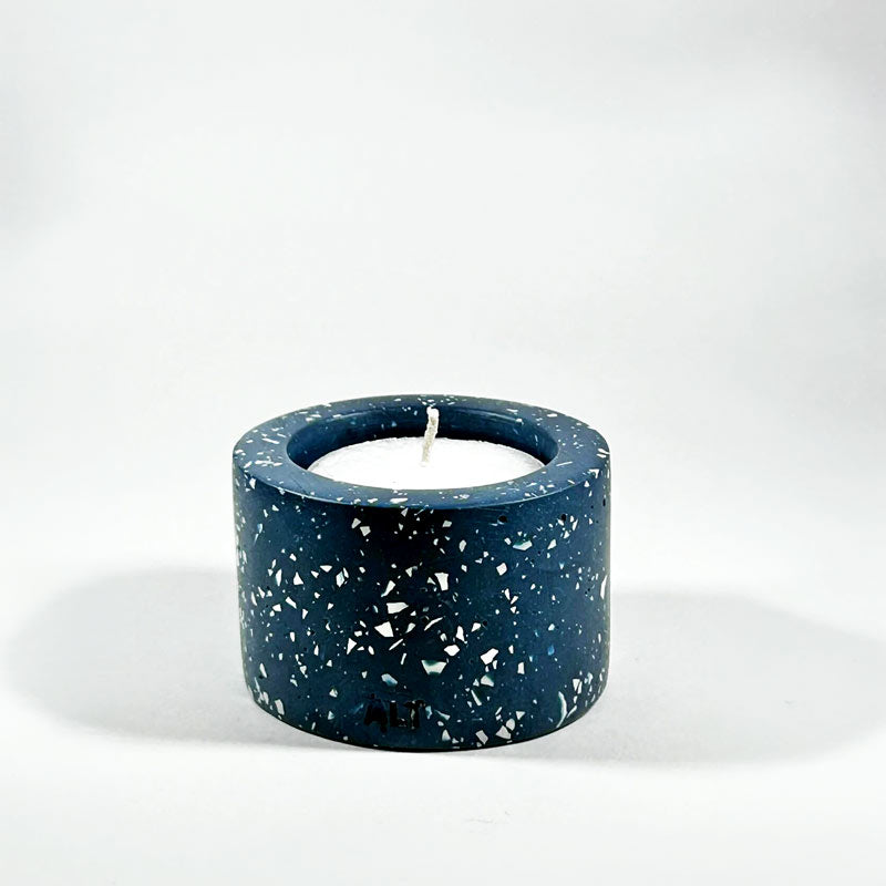 Navy blue terrazzo-patterned tealight candle holder with a white candle inside on a white background