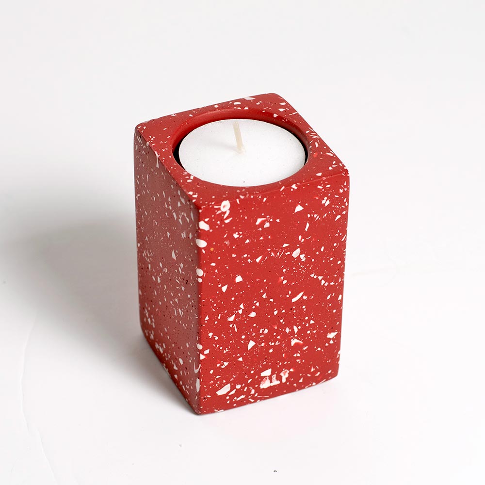 Red speckled candle holder with a white candle on a light gray background