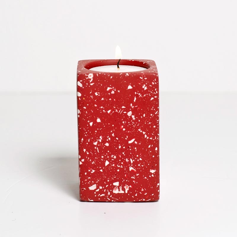 Red speckled candle holder with a white candle on a white background