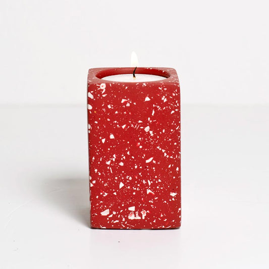 Red speckled candle holder with a white candle on a white background