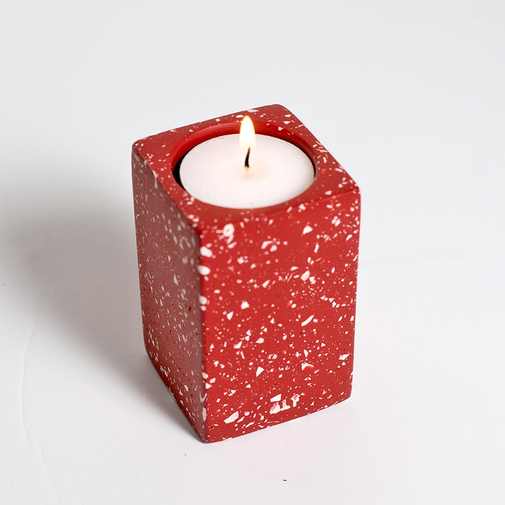 Red speckled candle holder with a white candle on a light gray background
