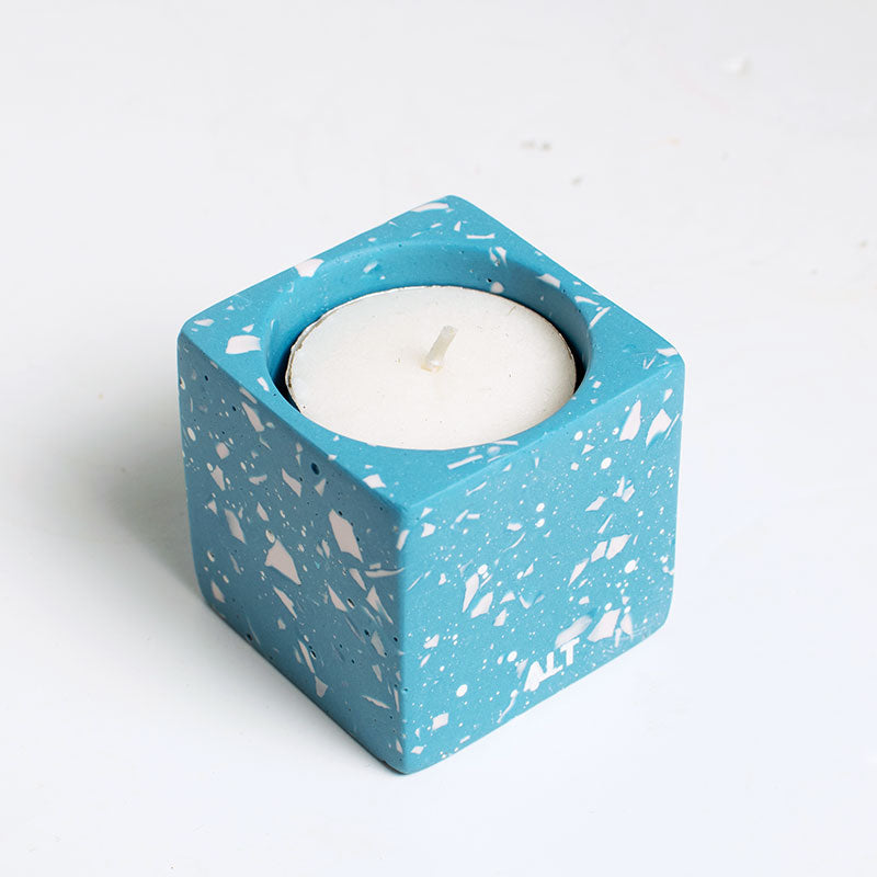 Light blue terrazzo candle holder with a white candle on a white background