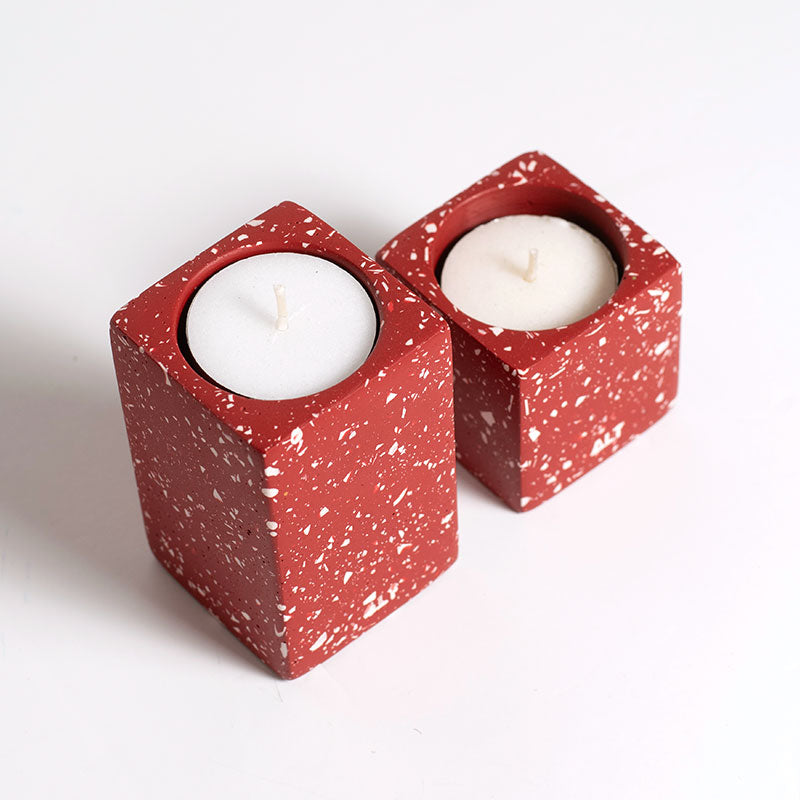 Two red terrazzo candle holders with white candles on a white background