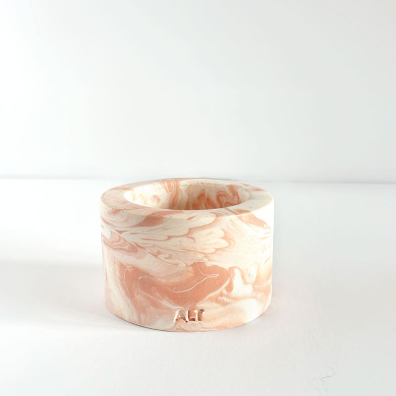 Marble-patterned salmon pink tealight candle holder on a white background