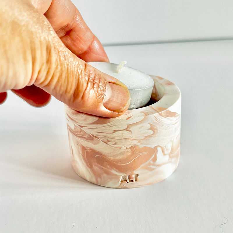 Marble-patterned salmon pink tealight candle holder with a hand placing a tea light inside on a light gray background