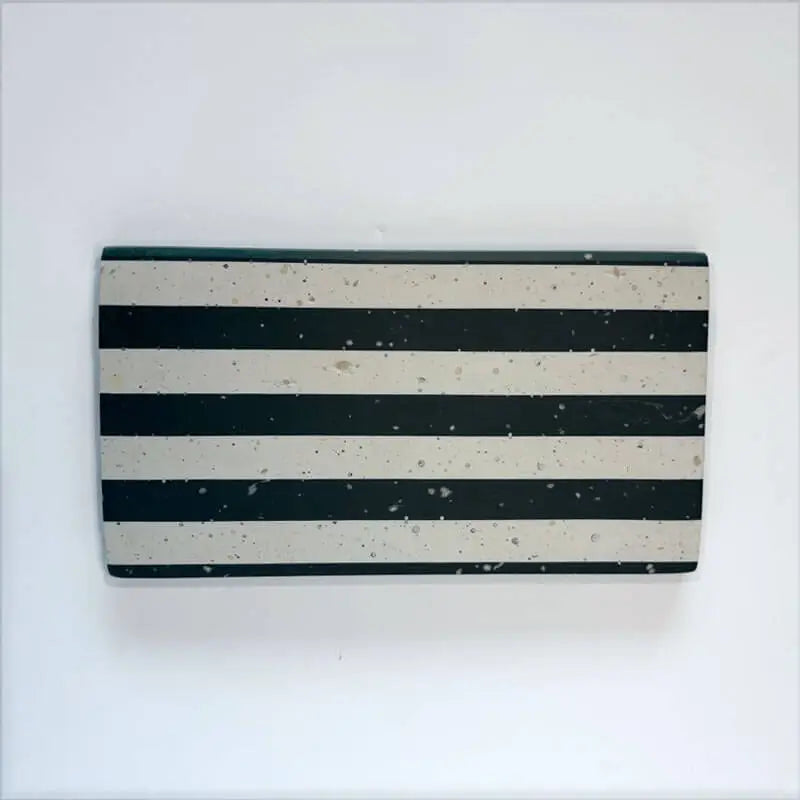 A rectangular tray with horizontal black and off-white stripes, featuring a speckled concrete-like texture, shown against a plain white background.