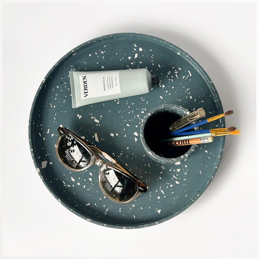 Round navy with white terrazzo Jesmonite decorative tray with a pen pot with some pencils, a pair of sunglasses and a hand cream on a white background