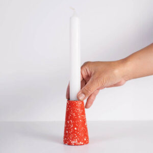 Hand-crafted red with white terrazzo taper candle holder - medium with a hand holding a white taper candle